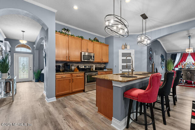 kitchen featuring stainless steel appliances, decorative light fixtures, sink, and a center island with sink