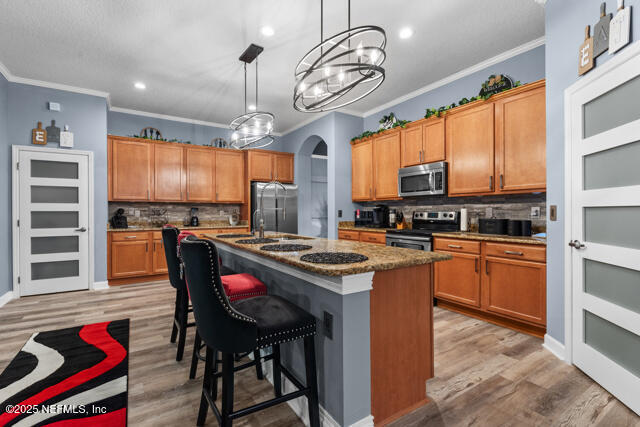 kitchen with pendant lighting, a kitchen breakfast bar, stainless steel appliances, a center island with sink, and light wood-type flooring