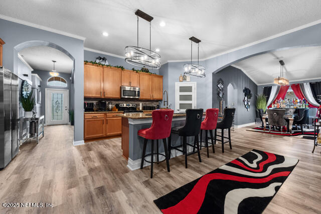 kitchen with a breakfast bar, appliances with stainless steel finishes, a kitchen island with sink, decorative light fixtures, and light wood-type flooring