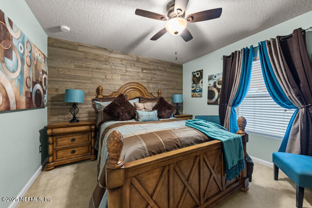 carpeted bedroom with ceiling fan, a textured ceiling, and wooden walls