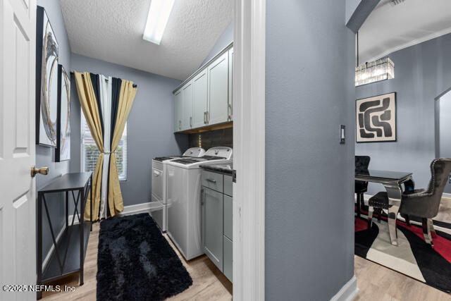 laundry room with cabinets, light wood-type flooring, a textured ceiling, and washer and clothes dryer