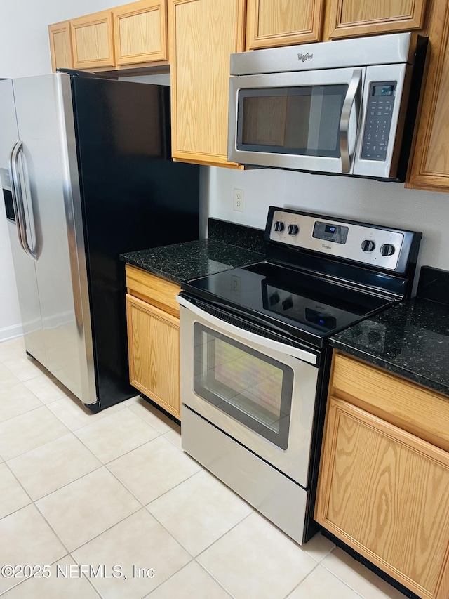 kitchen with stainless steel appliances, light tile patterned floors, light brown cabinets, and dark stone countertops