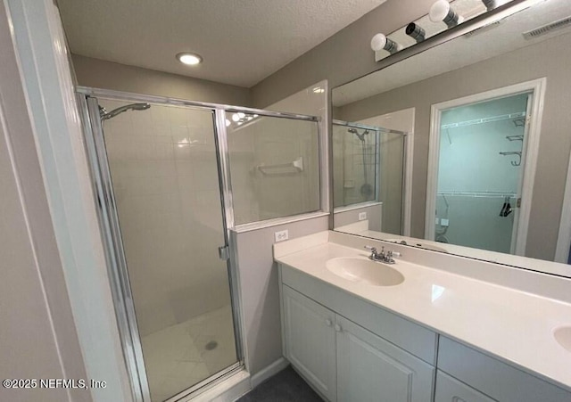 bathroom with a shower with door, vanity, and a textured ceiling