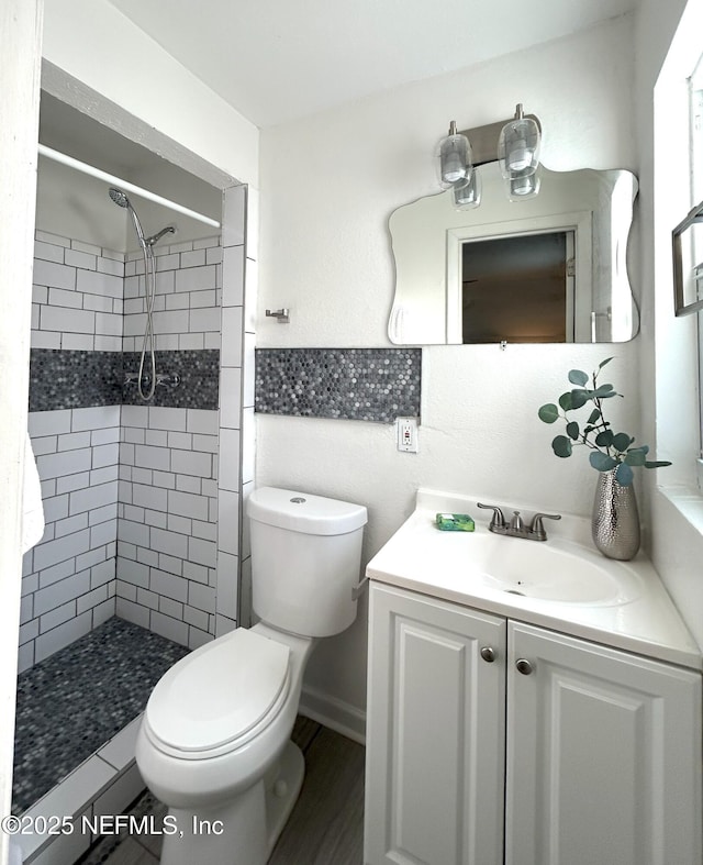 bathroom featuring a tile shower, vanity, and toilet