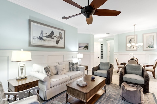 living area with a wainscoted wall, ceiling fan with notable chandelier, a decorative wall, crown molding, and tile patterned flooring