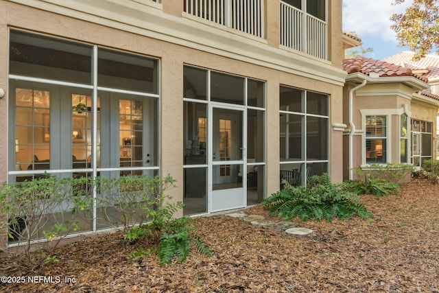 view of property exterior with stucco siding, a balcony, french doors, and a tiled roof