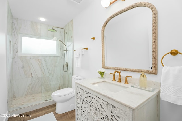 bathroom with wood-type flooring, tiled shower, vanity, and toilet