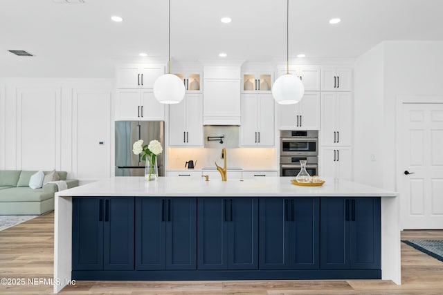 kitchen with appliances with stainless steel finishes, a large island, pendant lighting, and light hardwood / wood-style floors