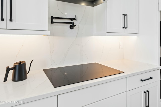 kitchen with backsplash, black electric stovetop, white cabinets, and light stone counters