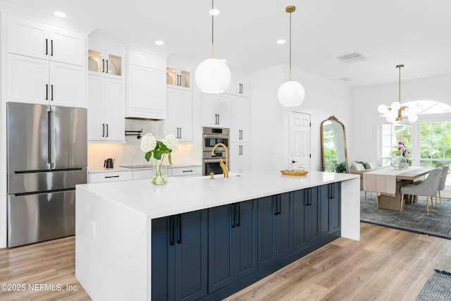 kitchen with hanging light fixtures, an island with sink, appliances with stainless steel finishes, and white cabinetry