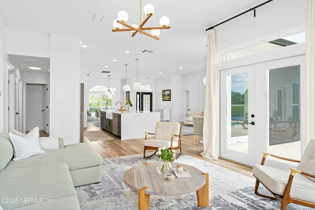 living room featuring an inviting chandelier, sink, light hardwood / wood-style flooring, and french doors