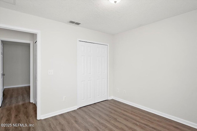 unfurnished bedroom with dark wood-type flooring, a closet, and a textured ceiling