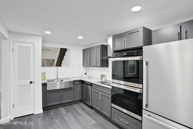 kitchen with appliances with stainless steel finishes, a sink, gray cabinetry, and tasteful backsplash