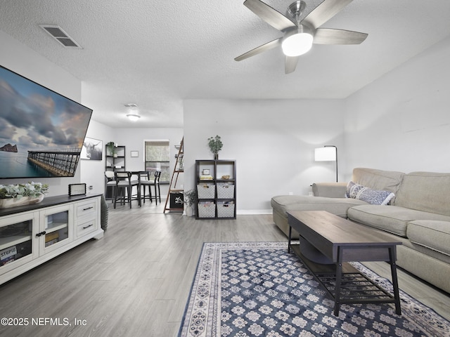 living room with hardwood / wood-style flooring, ceiling fan, and a textured ceiling