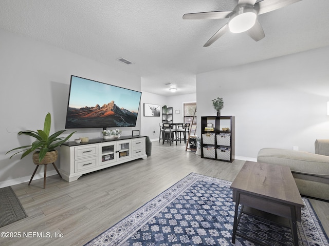 living room with ceiling fan, light hardwood / wood-style flooring, and a textured ceiling