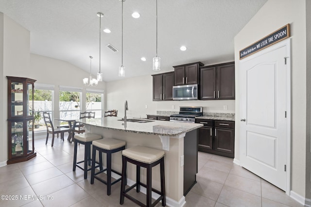 kitchen featuring a breakfast bar area, a kitchen island with sink, stainless steel appliances, a sink, and hanging light fixtures