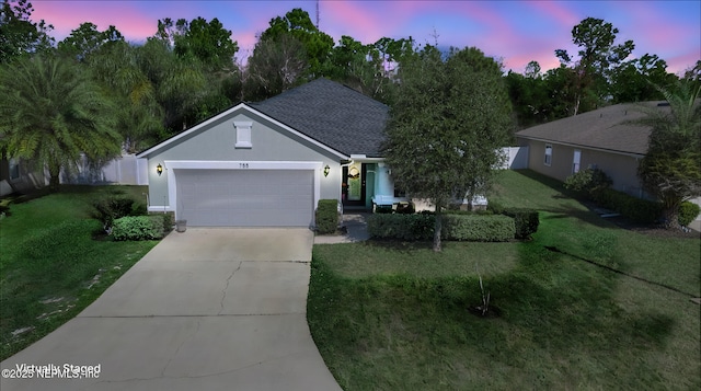 ranch-style house featuring concrete driveway, roof with shingles, an attached garage, a front yard, and stucco siding