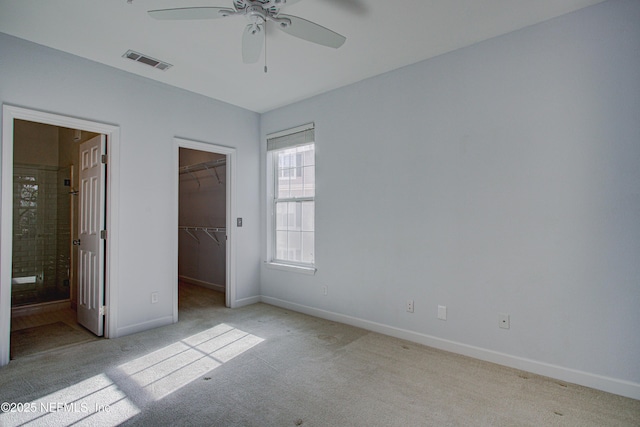 unfurnished bedroom with a closet, ensuite bath, ceiling fan, light carpet, and a walk in closet