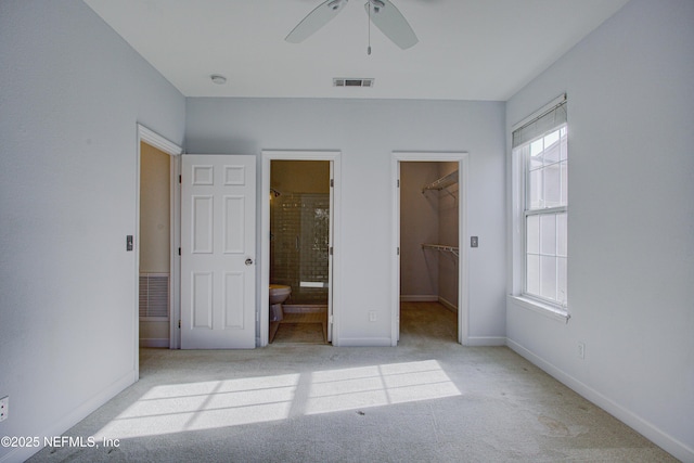 unfurnished bedroom featuring a spacious closet, a closet, ceiling fan, light carpet, and ensuite bathroom