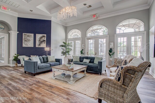 living room featuring hardwood / wood-style floors, decorative columns, ornamental molding, french doors, and a high ceiling