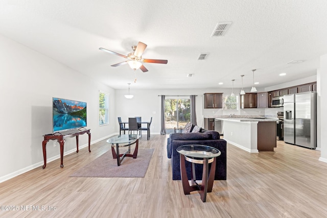 living room featuring ceiling fan, light hardwood / wood-style floors, and a textured ceiling