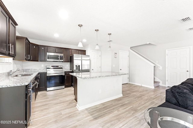 kitchen with sink, light hardwood / wood-style flooring, stainless steel appliances, a center island, and decorative light fixtures