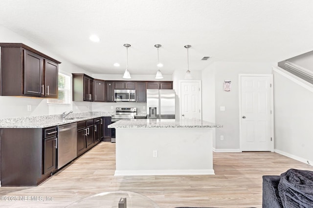 kitchen featuring decorative light fixtures, a center island, dark brown cabinets, stainless steel appliances, and light stone countertops