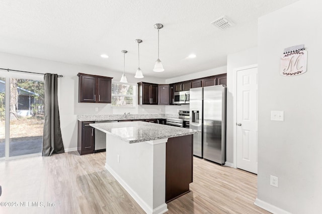 kitchen with hanging light fixtures, stainless steel appliances, dark brown cabinetry, light hardwood / wood-style floors, and a kitchen island