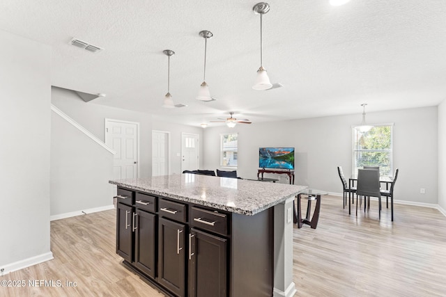 kitchen with dark brown cabinetry, hanging light fixtures, light hardwood / wood-style flooring, and light stone countertops