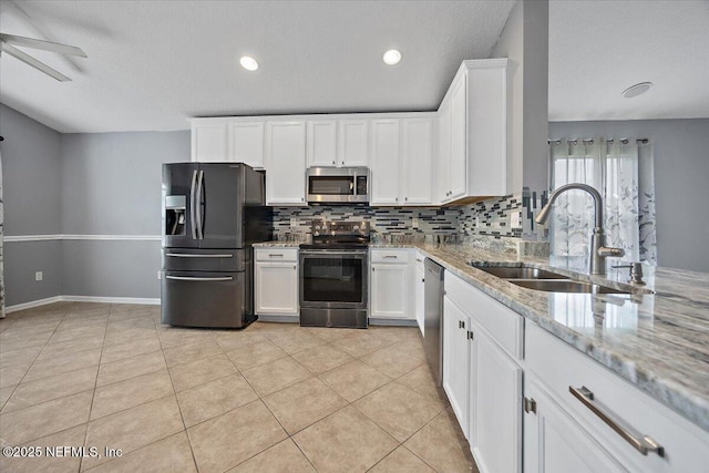 kitchen featuring light tile patterned flooring, appliances with stainless steel finishes, sink, white cabinets, and light stone countertops