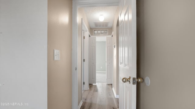 hallway with a textured ceiling and light hardwood / wood-style floors