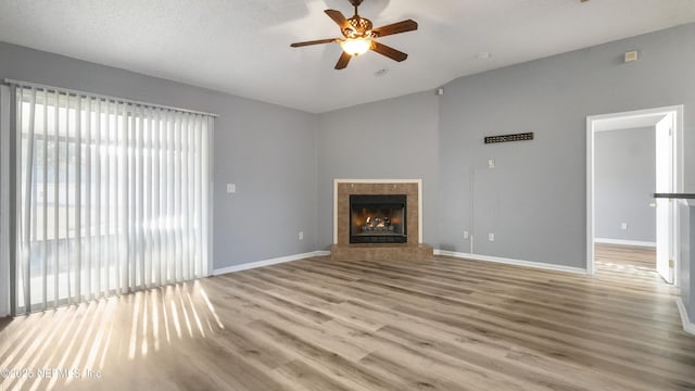 unfurnished living room with ceiling fan, a textured ceiling, a tile fireplace, and light wood-type flooring