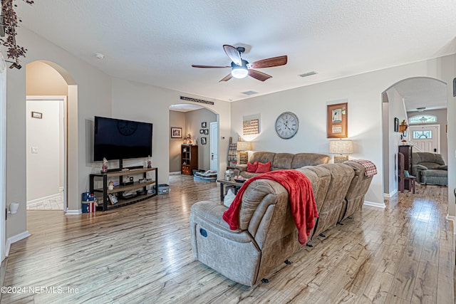 living room featuring ceiling fan, a textured ceiling, and light wood-type flooring