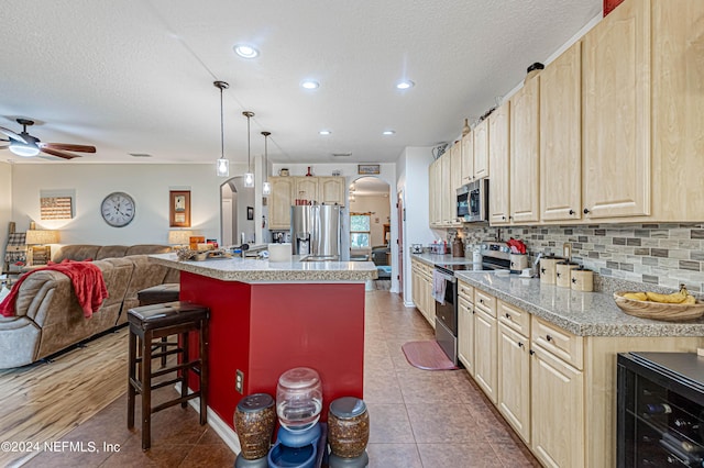 kitchen featuring pendant lighting, appliances with stainless steel finishes, a kitchen breakfast bar, wine cooler, and an island with sink