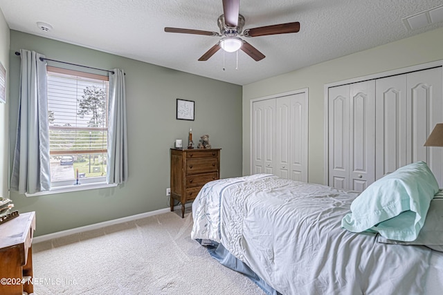 carpeted bedroom featuring ceiling fan, two closets, and a textured ceiling