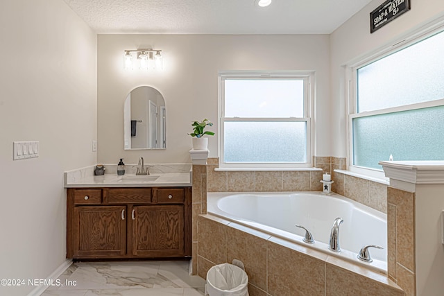 bathroom with vanity, tiled tub, and a textured ceiling