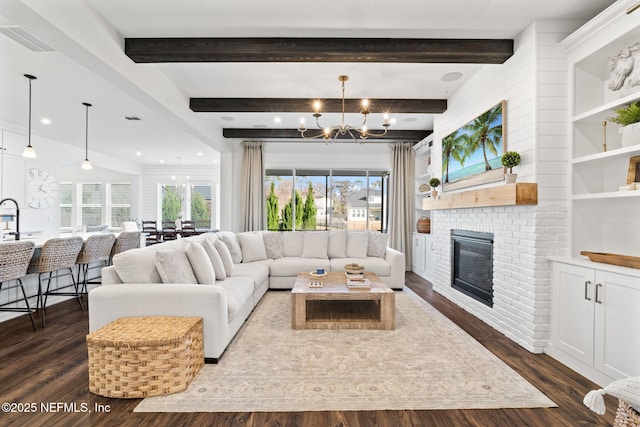 living room featuring an inviting chandelier, a brick fireplace, beam ceiling, and dark hardwood / wood-style flooring