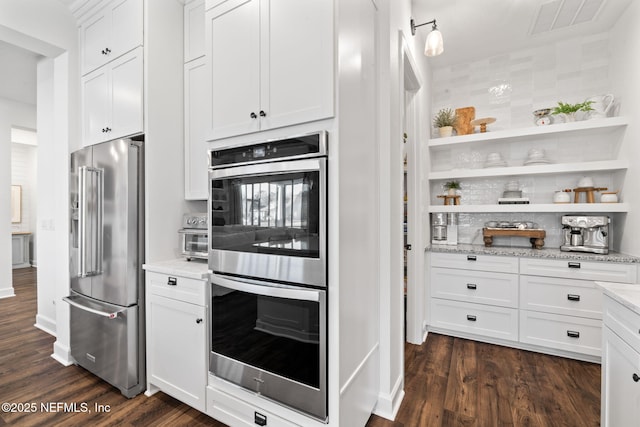 kitchen with appliances with stainless steel finishes, dark hardwood / wood-style floors, white cabinets, and light stone counters