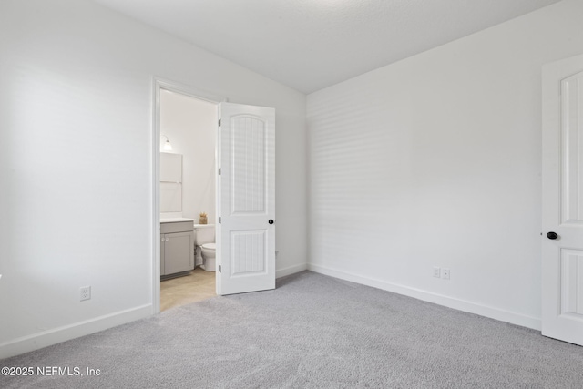 unfurnished bedroom featuring ensuite bathroom, lofted ceiling, and light carpet