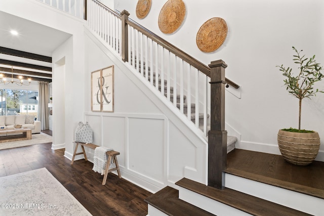 stairs with hardwood / wood-style flooring, a chandelier, and beamed ceiling