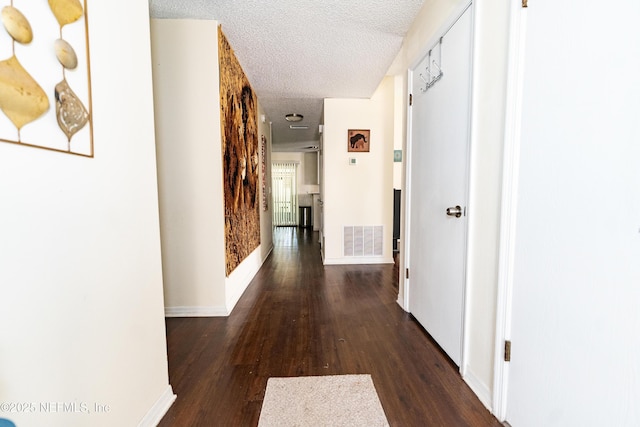 corridor featuring baseboards, wood finished floors, visible vents, and a textured ceiling