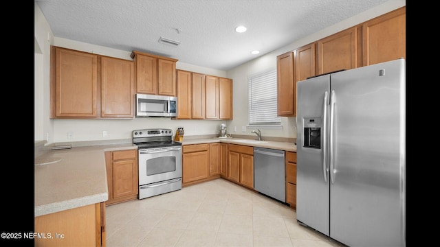 kitchen with light tile patterned flooring, appliances with stainless steel finishes, sink, and a textured ceiling