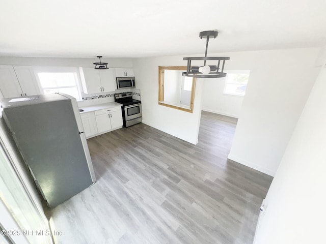 kitchen with an inviting chandelier, light wood-type flooring, appliances with stainless steel finishes, pendant lighting, and white cabinets