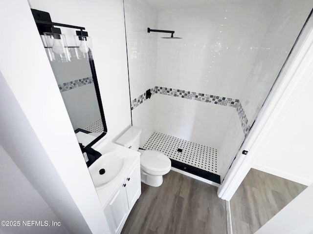 bathroom featuring wood-type flooring, a tile shower, vanity, and toilet