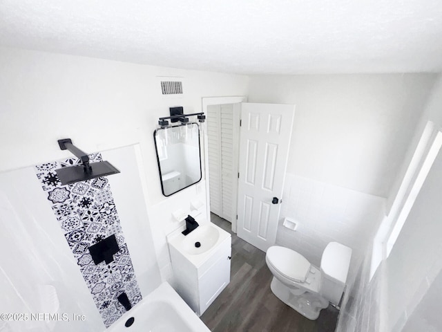 bathroom featuring wood-type flooring, toilet, vanity, and tile walls