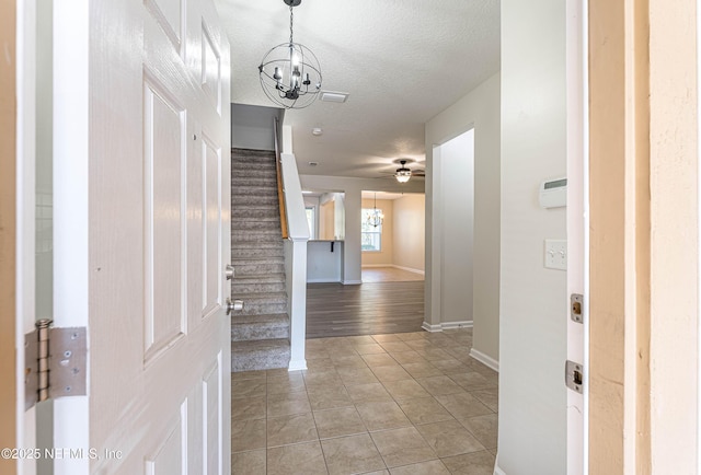 tiled foyer entrance featuring ceiling fan with notable chandelier and a textured ceiling