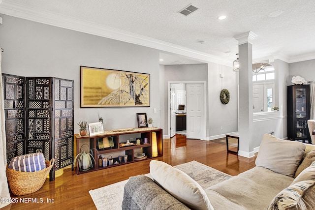 living room featuring a textured ceiling, baseboards, wood finished floors, visible vents, and ornamental molding