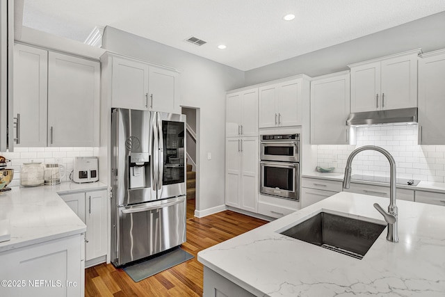 kitchen with white cabinets, appliances with stainless steel finishes, a sink, under cabinet range hood, and visible vents