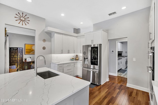 kitchen featuring light stone countertops, a sink, stainless steel appliances, decorative backsplash, and dark wood-type flooring