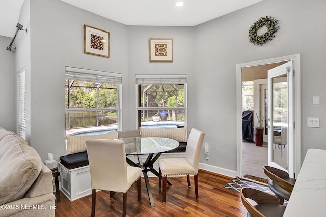 dining area with recessed lighting, baseboards, wood finished floors, and a high ceiling